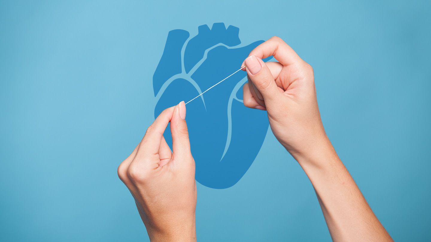 hands holding string of floss in front of blue anatomical heart shaped icon
